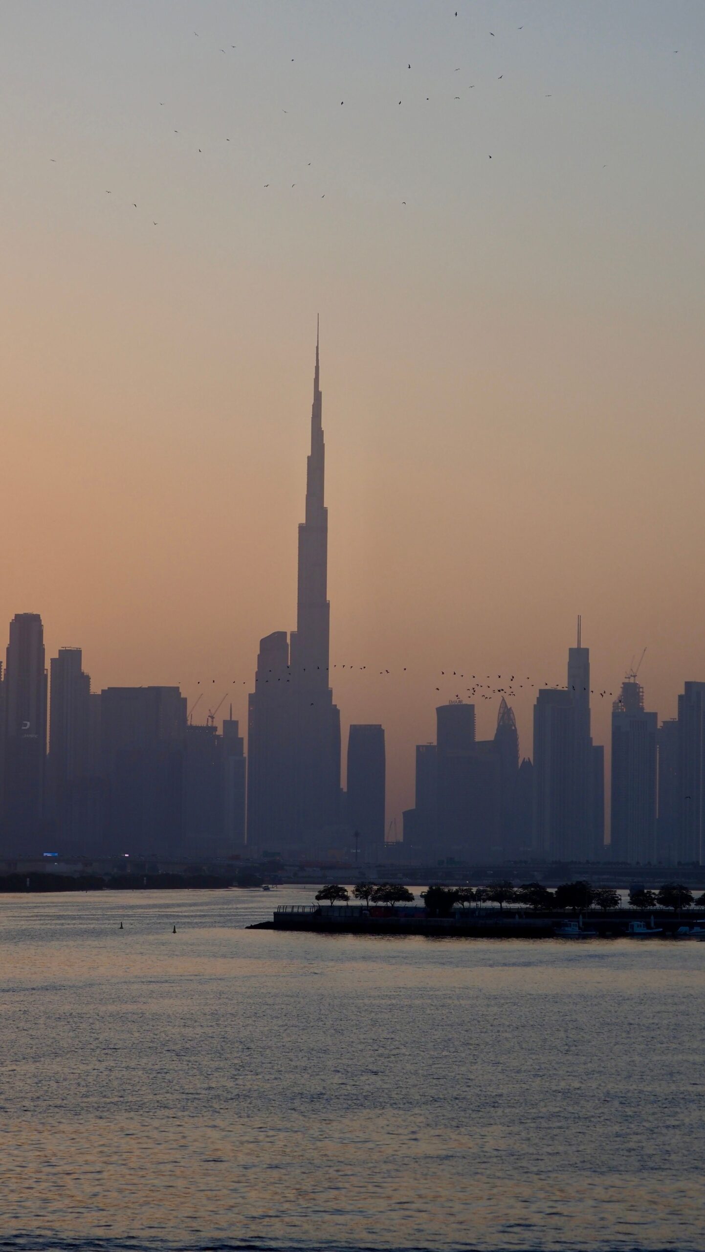 Stunning view of the Dubai skyline and Burj Khalifa at sunset over a calm waterfront.