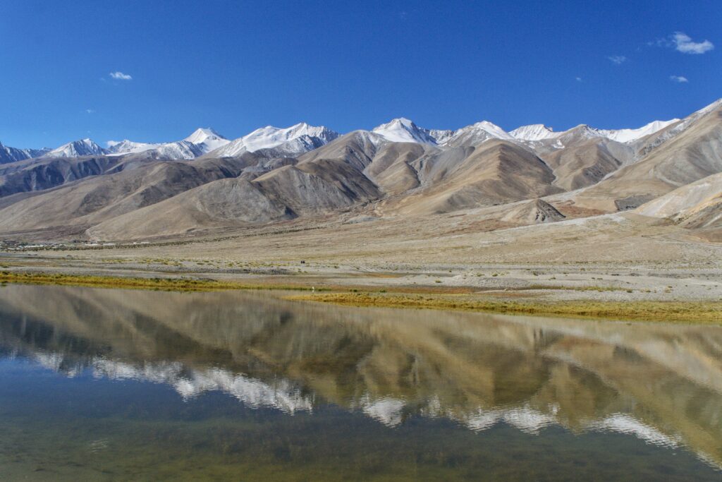 Majestic snowcapped mountains reflecting in a tranquil lake under a clear blue sky.